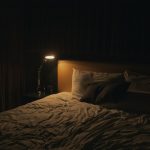 A bedside lamp glowing next to a made bed at night