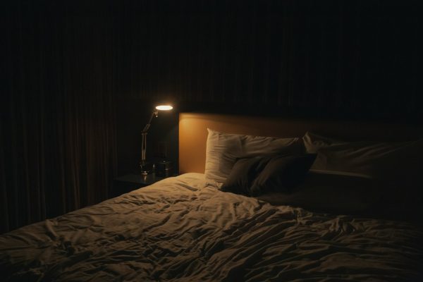 A bedside lamp glowing next to a made bed at night