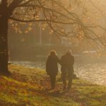 An adult couple walking beside a river at sunset