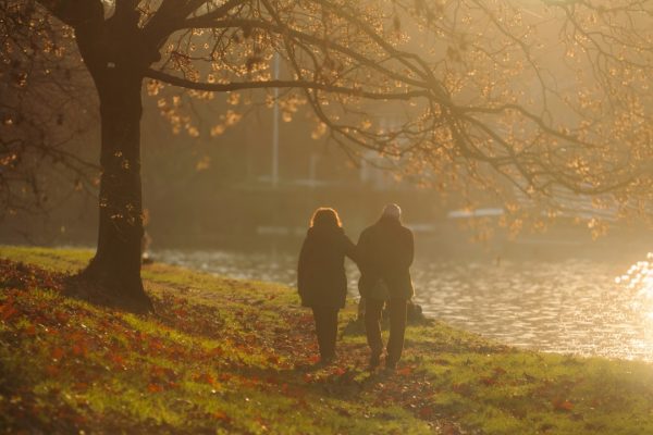 An adult couple walking beside a river at sunset