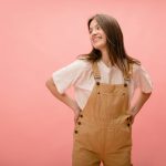 A woman standing confidently in overalls with her hands on her hips