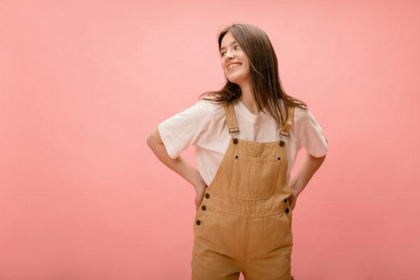A woman standing confidently in overalls with her hands on her hips